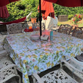 Outdoor dining table with lemon print oilcloth tablecloth, surrounded by ornate chairs under a red umbrella, perfect for events or garden gatherings.